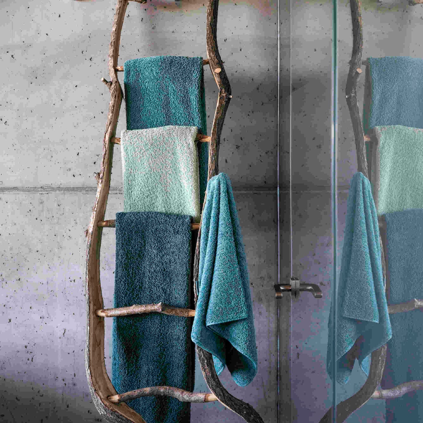 Abyss & Habidecor Super Pile Towels In blue/green, hanging on rustic log rack