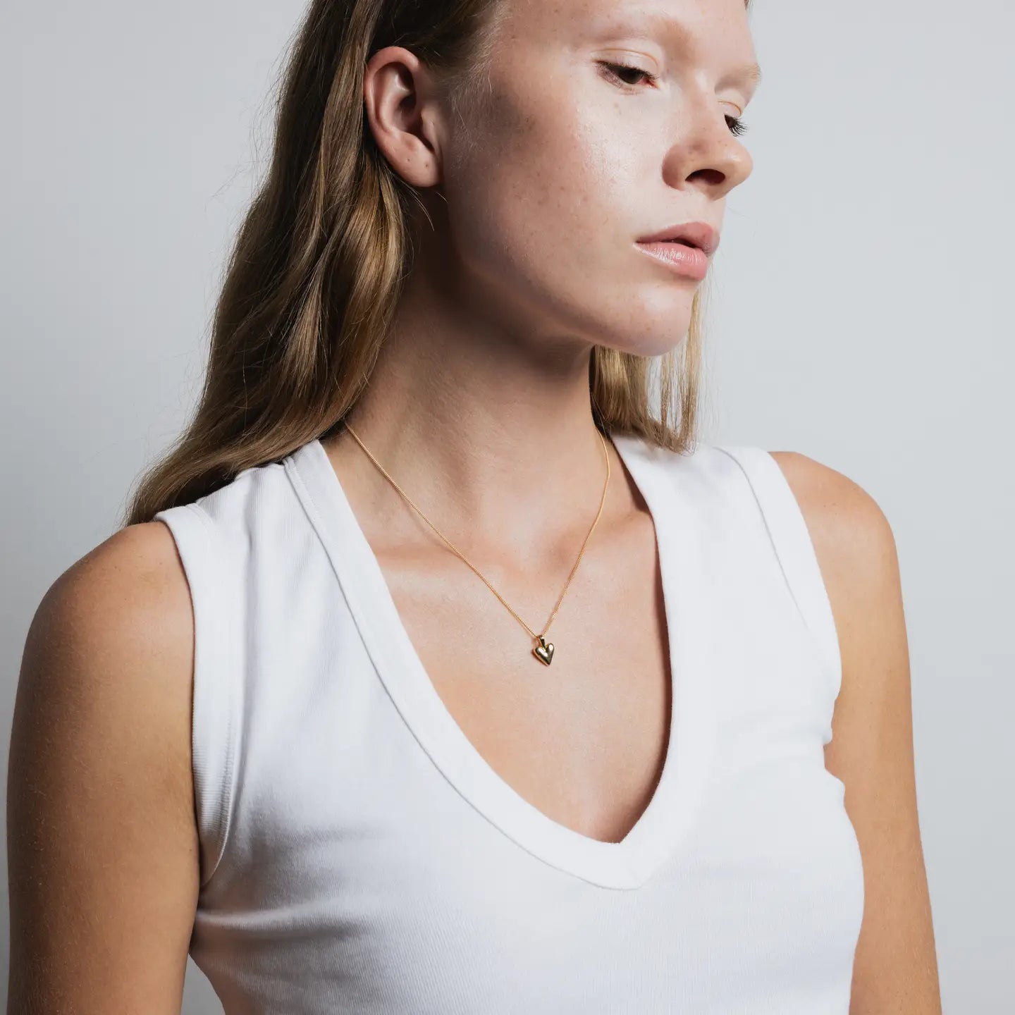 Woman wearing a white tank top and gold necklace against a plain background