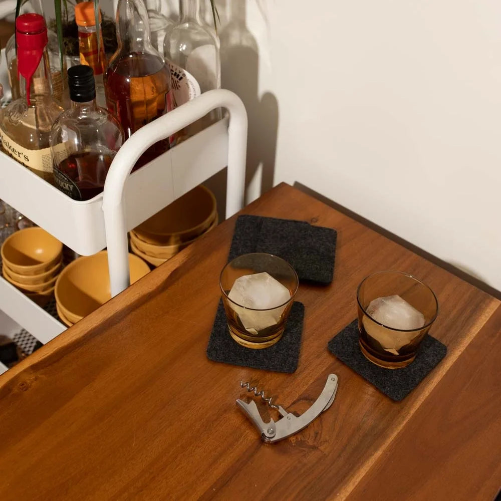 Bar cart with bottles, glasses, and wool coasters on a wooden surface.