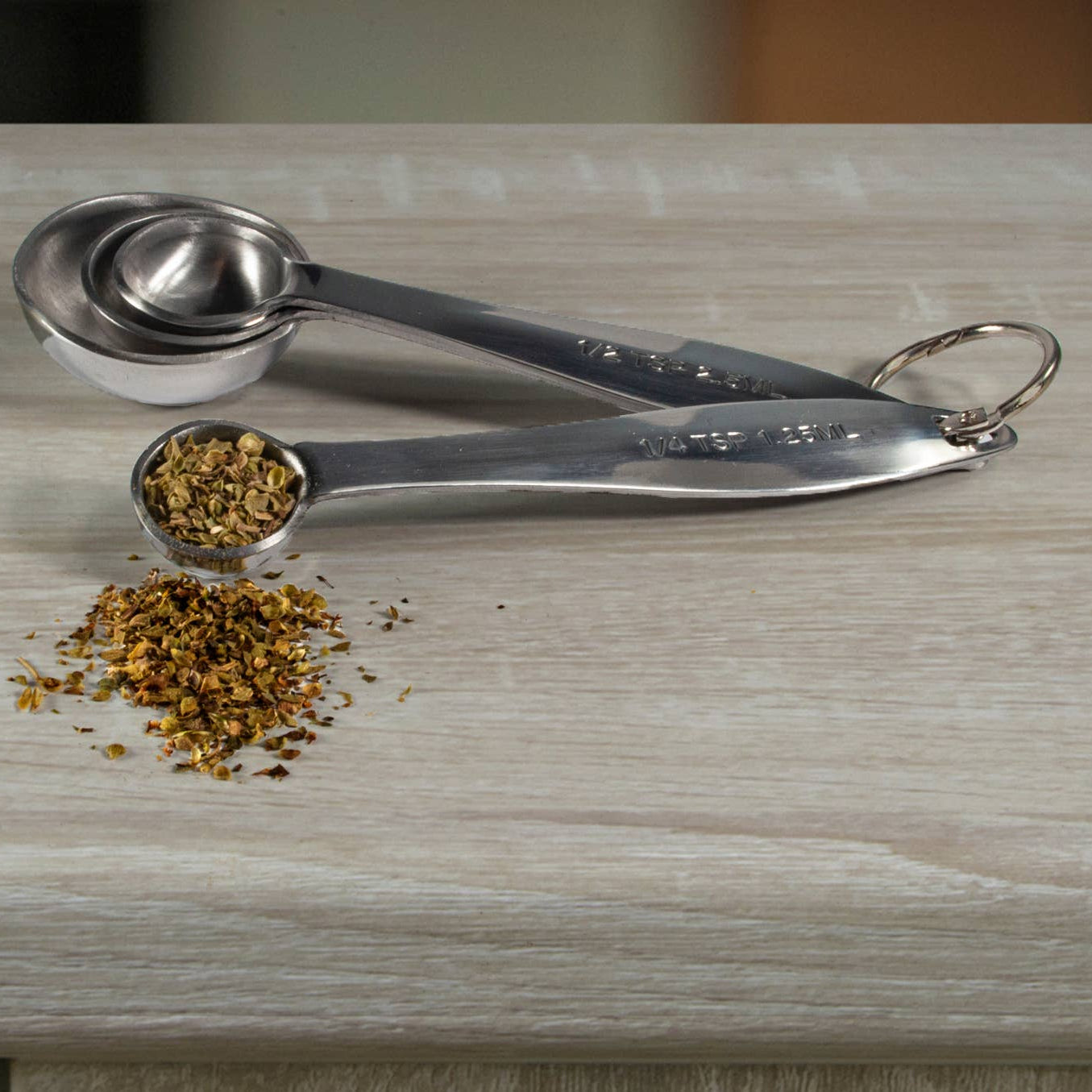 Set of metal measuring spoons with dried herbs on a wooden surface