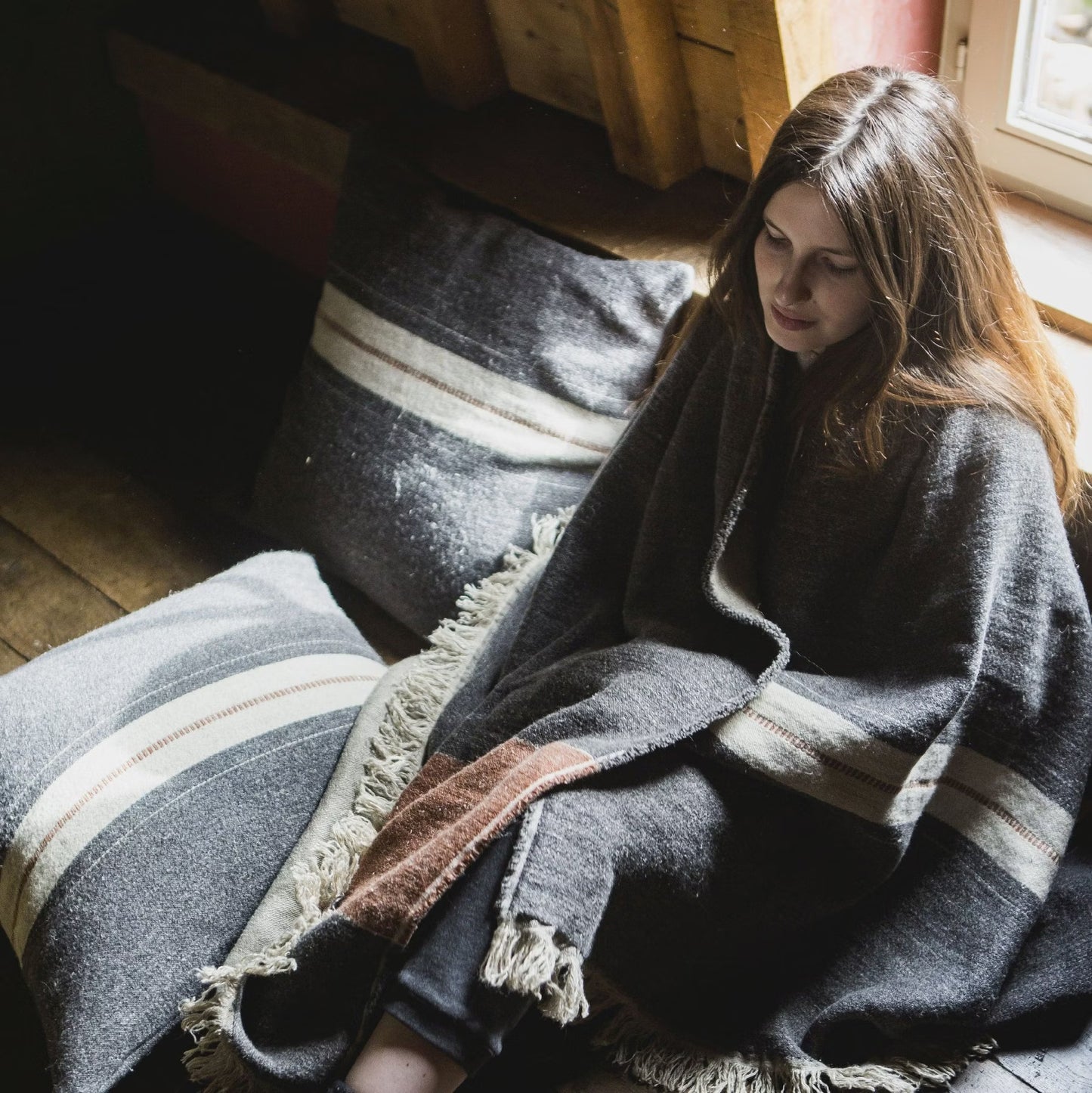 Woman sitting on a wooden floor wrapped in Libeco Luc Linen/Wool Throw Blanket