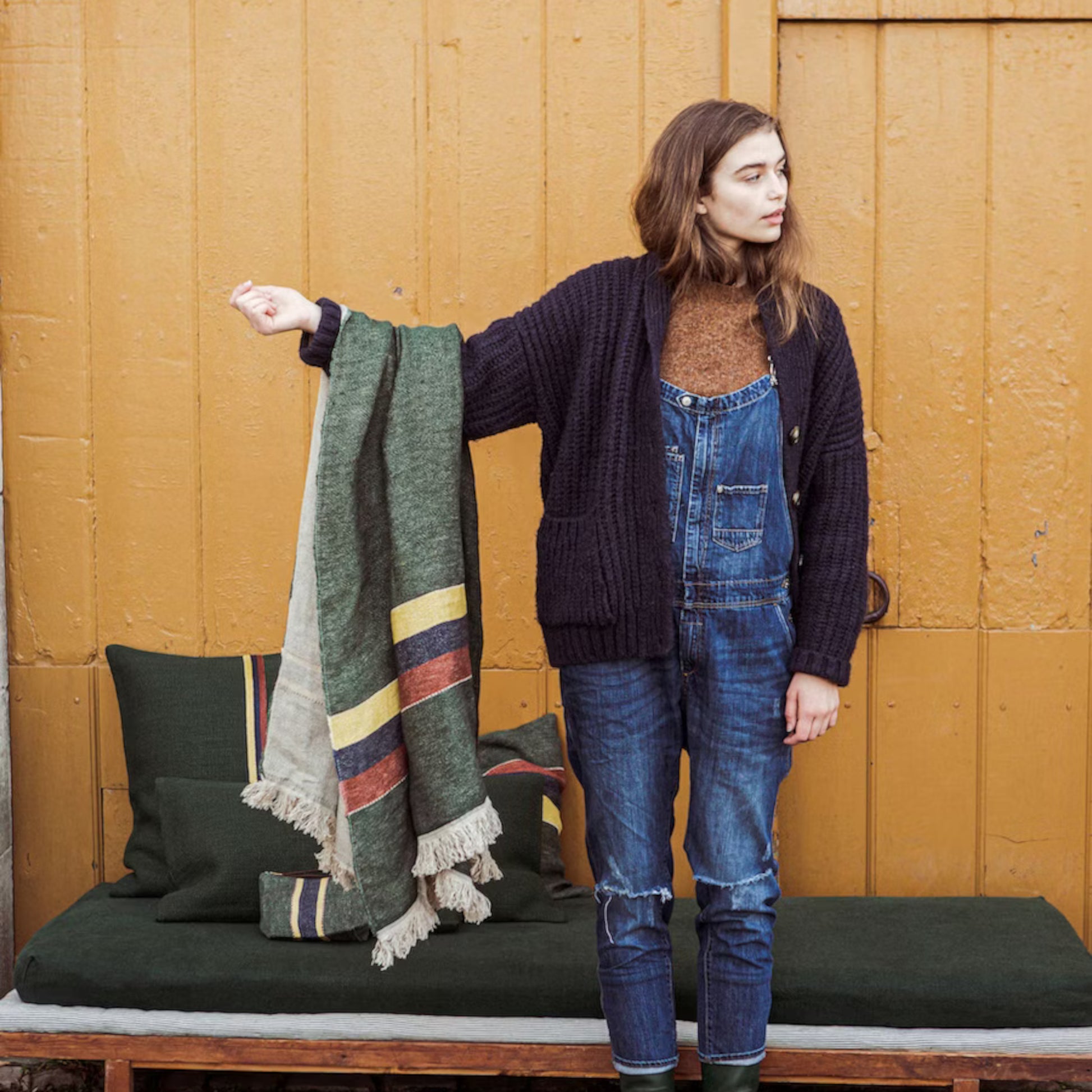 Woman holding Libeco The Belgian Towel Fouta in Spruce against a wooden wall.