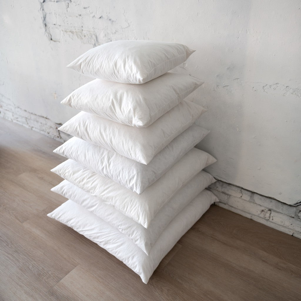 Stack of white pillows on a wooden floor against a white wall