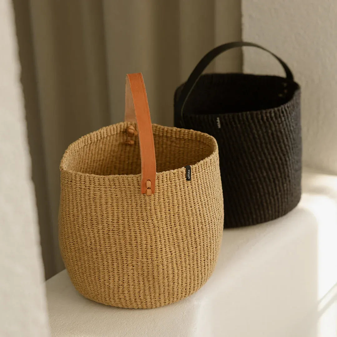 Two woven baskets with leather handles on a light surface.