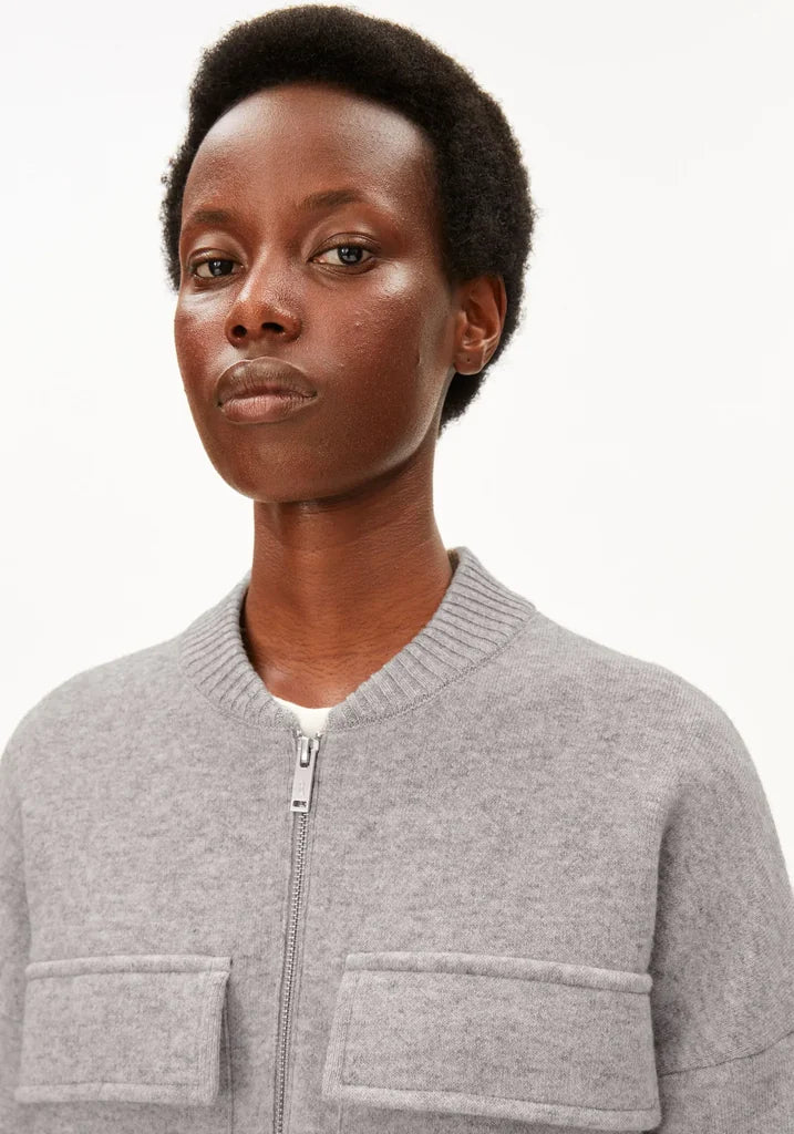 A close-up shot of a model wearing a light gray zip-up bomber jacket with two front patch pockets, set against a plain white studio background.