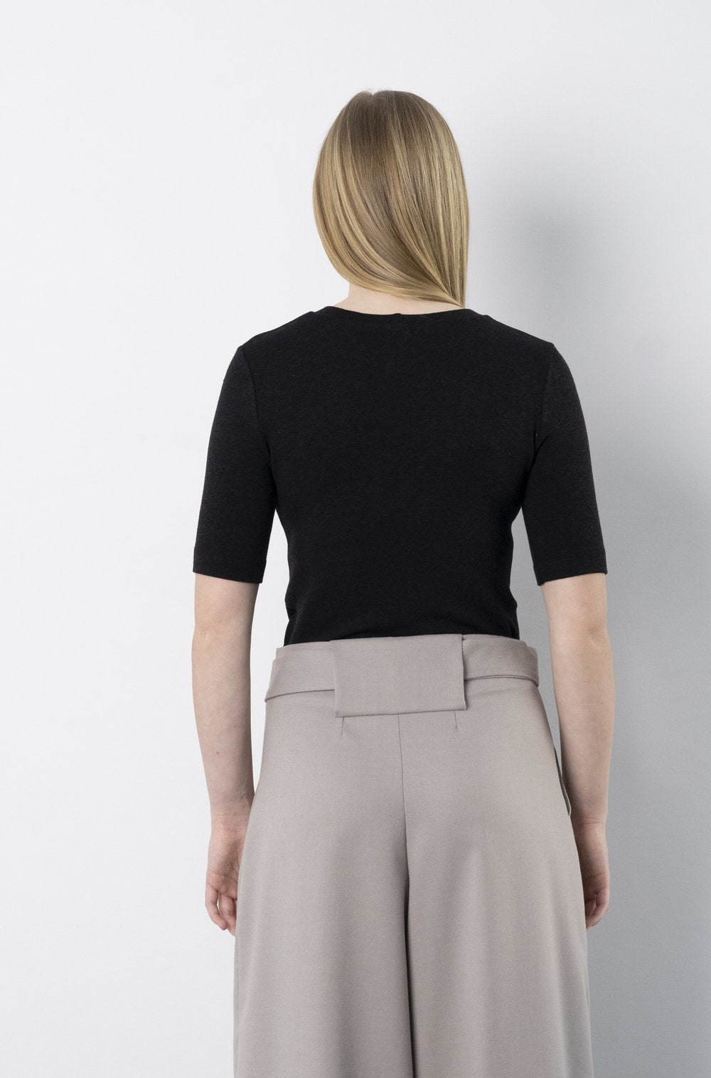 Back view of model wearing BodyBag by Jude black short sleeve top tucked into high waist gray wide leg trousers in Kelowna