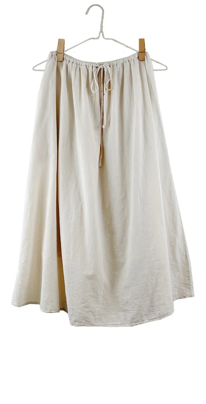 It Is Well L.A Canada Everyday Skirt in Natural hanging from a wire hanger with wooden clips, showing the cream cotton gauze, the drawstring ties and the gathered waist against a white background.