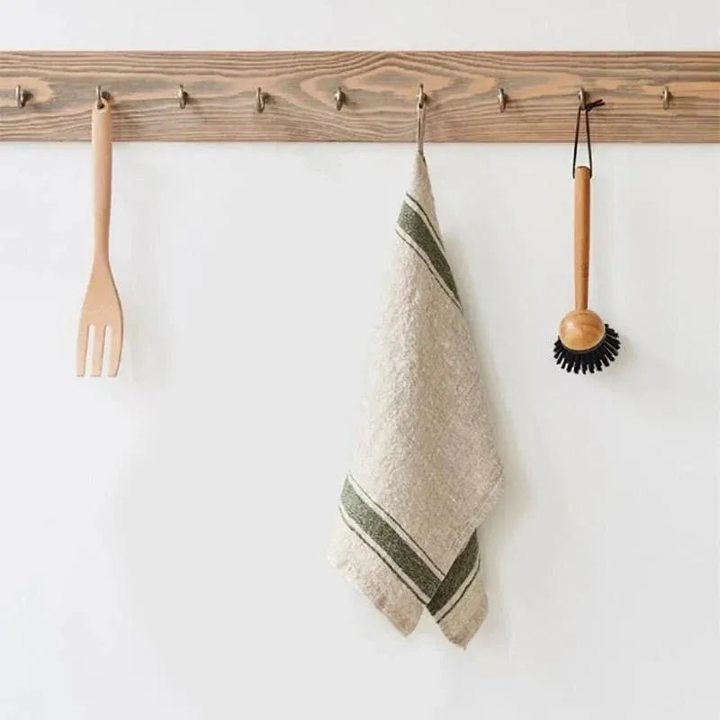Wooden towel rack with a towel, fork, and scrubber on a white wall