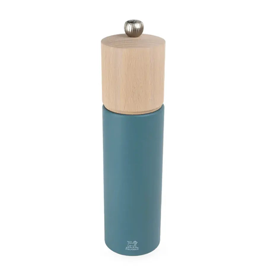 A modern cylindrical pepper mill with a matte teal blue body and a natural light wood grain top, featuring a small silver metal knob on the lid.