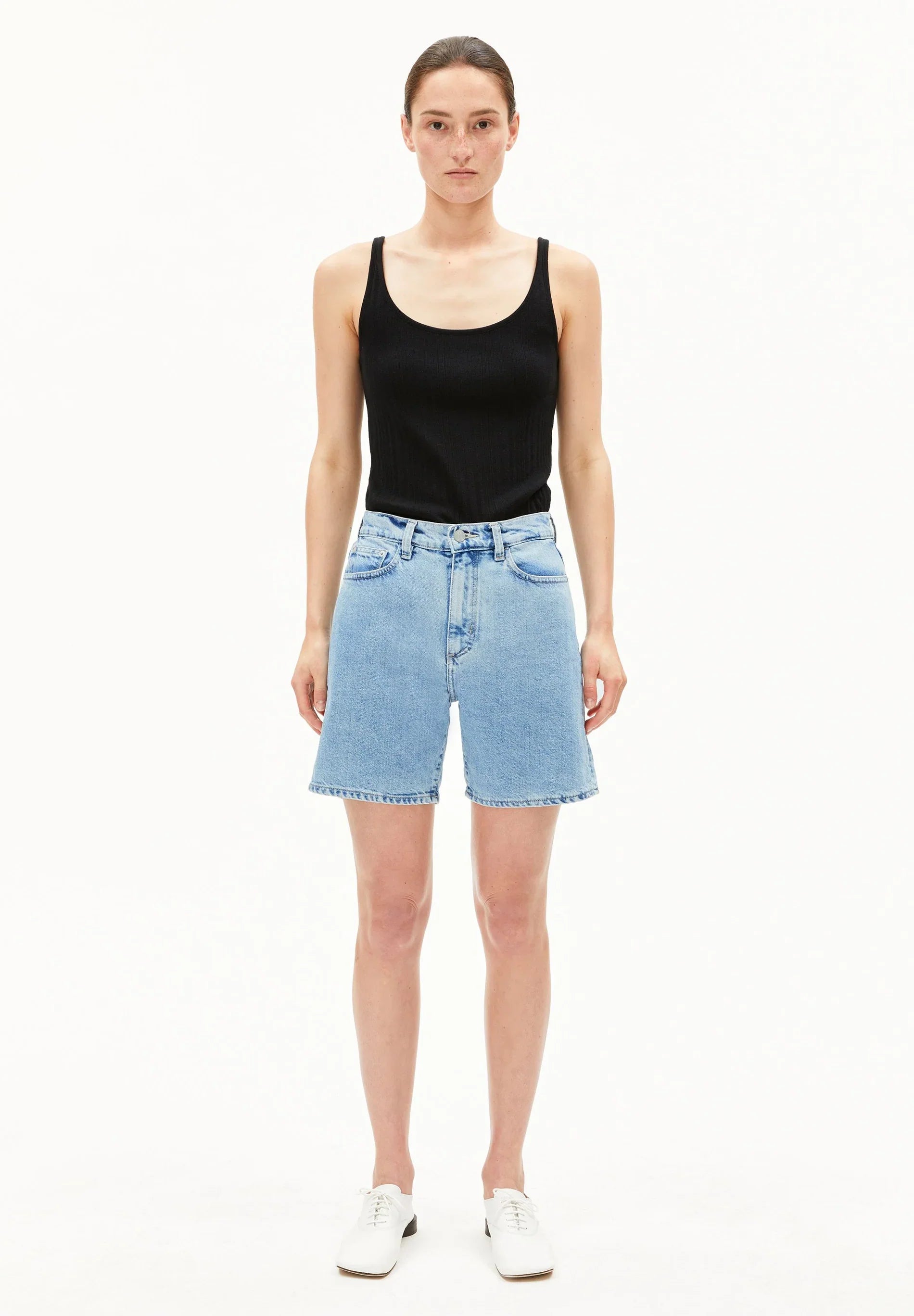 Woman wearing a black tank top and light blue denim shorts on a white background for Kelowna and Canada