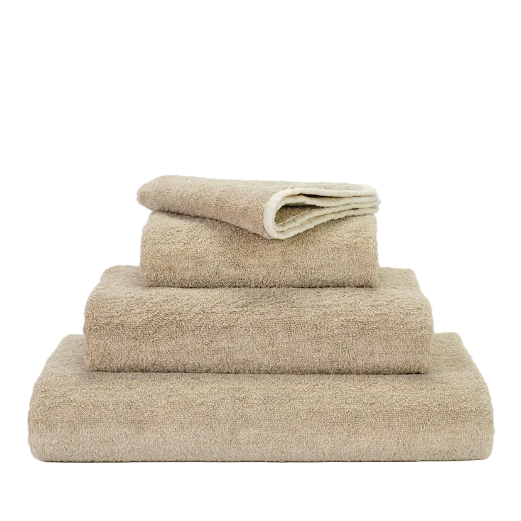 A stack of ecru colored bath towels with a plush texture, displayed against a white background.