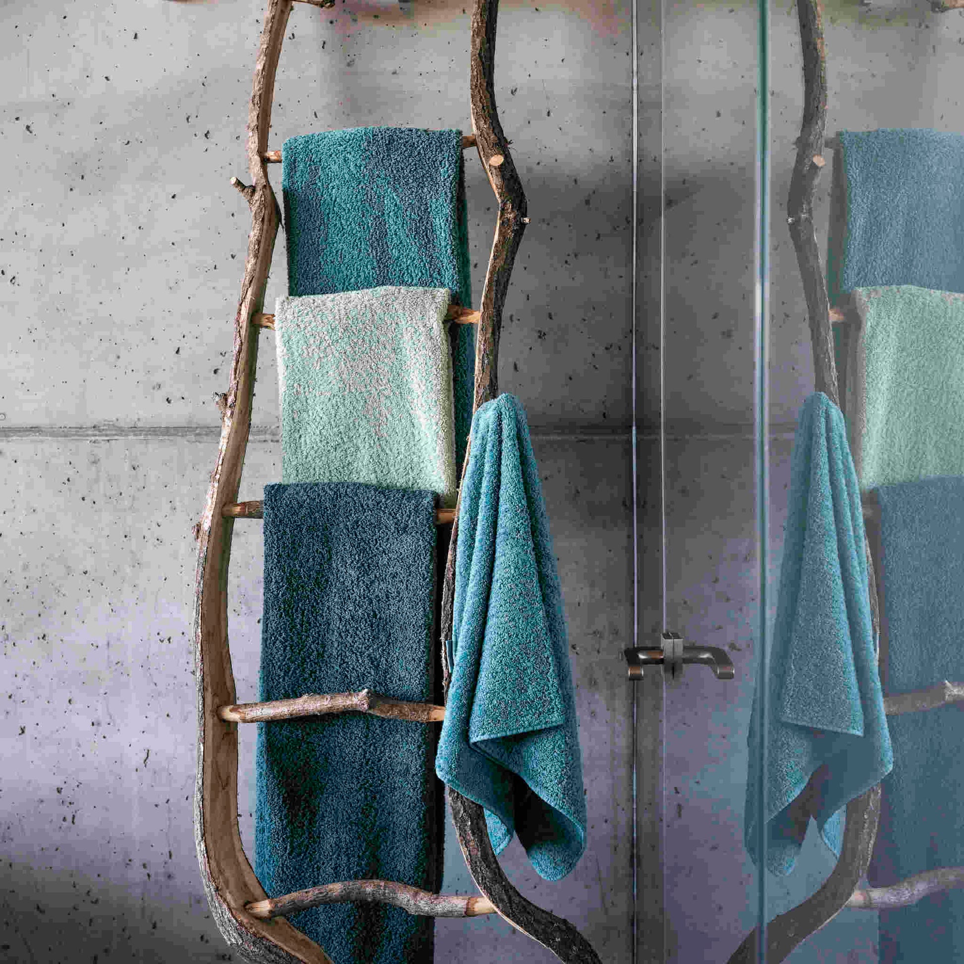 Abyss & Habidecor Super Pile Towels In blue/green, hanging on rustic log rack