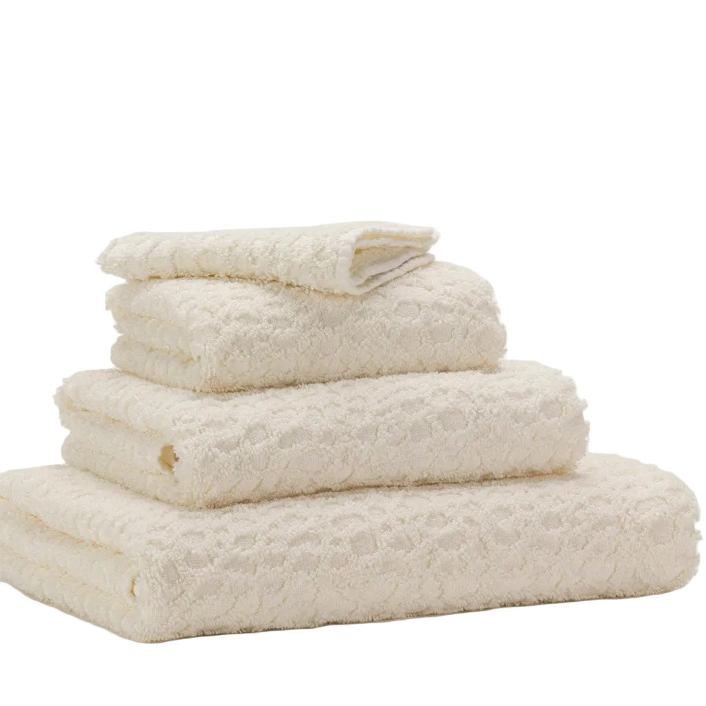 A stack of four folded textured cotton towels in a warm off-white or cream color, arranged by size on a seamless light background.