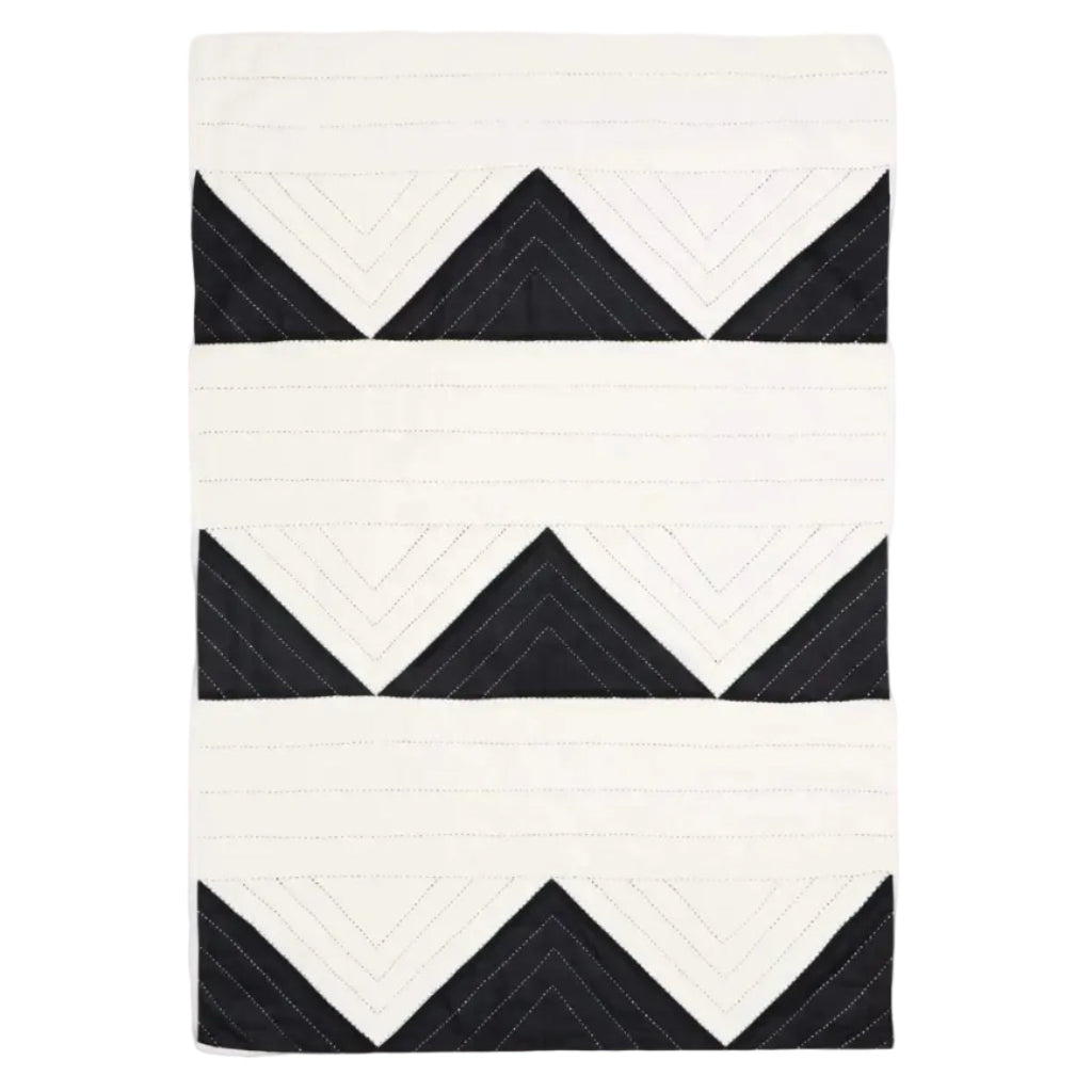 A rectangular quilted textile with a geometric pattern of black and off-white stitched triangles and chevron shapes, shown flat against a light gray background.