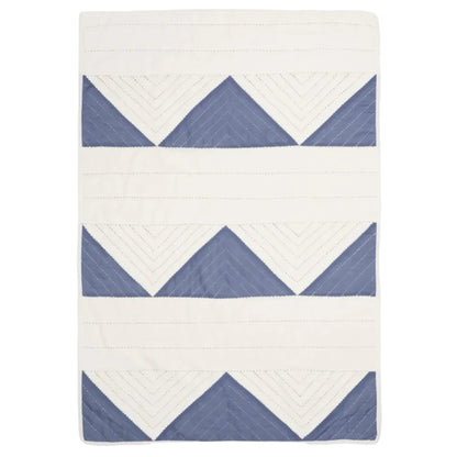 A rectangular quilted blanket featuring a geometric pattern of blue triangles and white chevron lines on an off-white background, shown flat against a light gray studio backdrop.