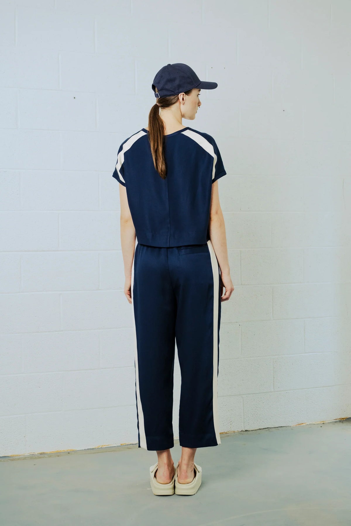 Person wearing a navy tracksuit with white stripes against a plain background