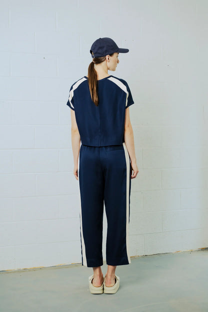 Person wearing a navy tracksuit with white stripes against a plain background