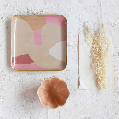 Decorative tray with abstract design, small container, and dried grass on a textured white surface