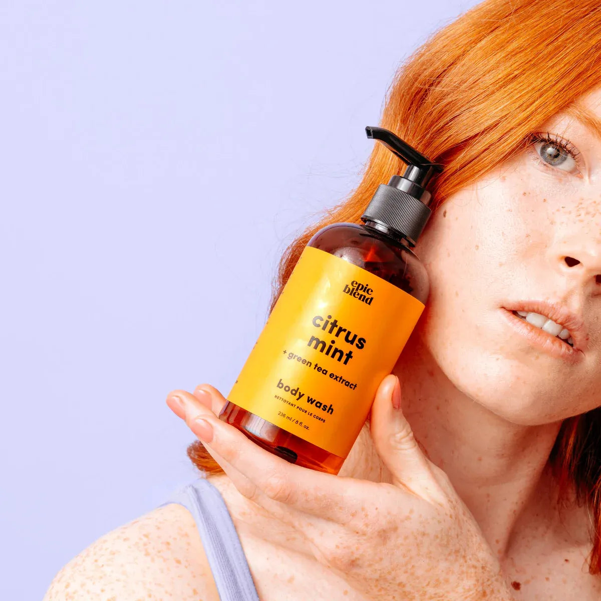 Person holding a bottle of 'epic blend' citrus mint body wash against a light purple background