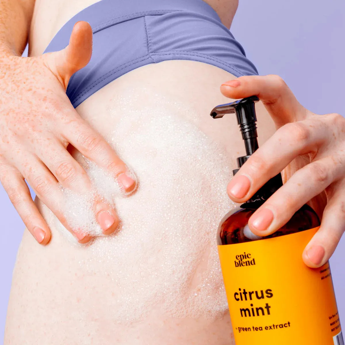 Person applying a bottle labeled 'epic blend' citrus mint body wash to their skin.