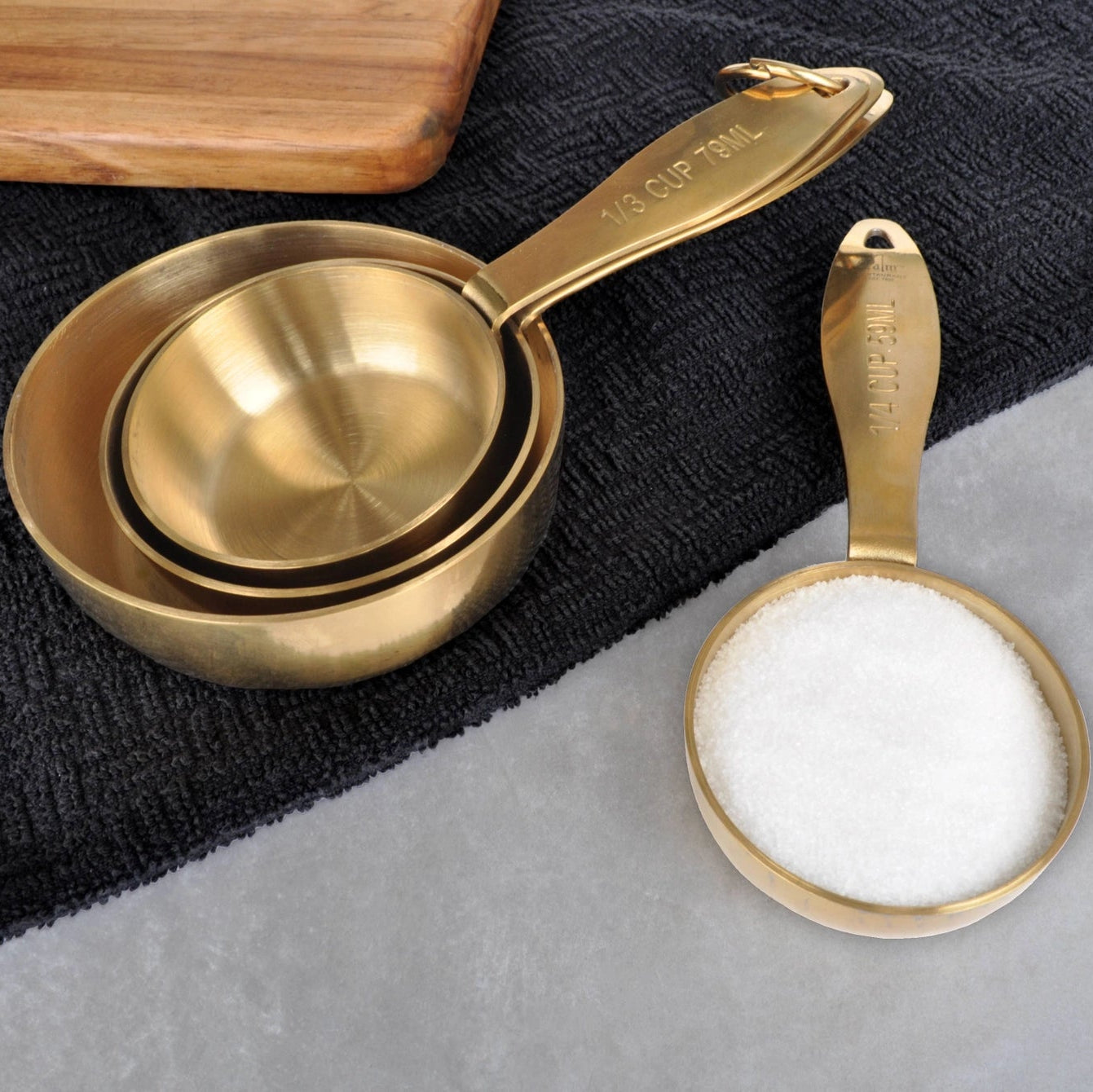 A set of gold-colored stainless steel measuring cups, including a 1/4 cup, 1/3 cup, 1/2 cup, and 1 cup size, displayed with a removable ring.
