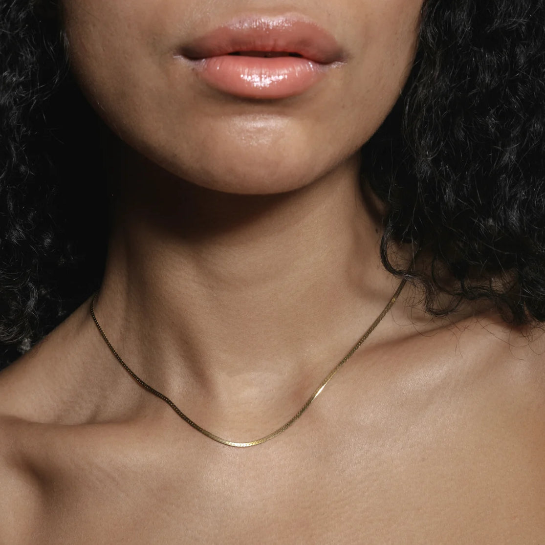 Close-up of a person wearing a thin gold necklace with a dark background