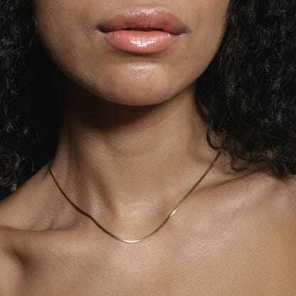 Close-up of a person wearing a thin gold necklace with a dark background