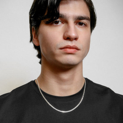 Man wearing a black shirt and silver chain necklace against a plain background