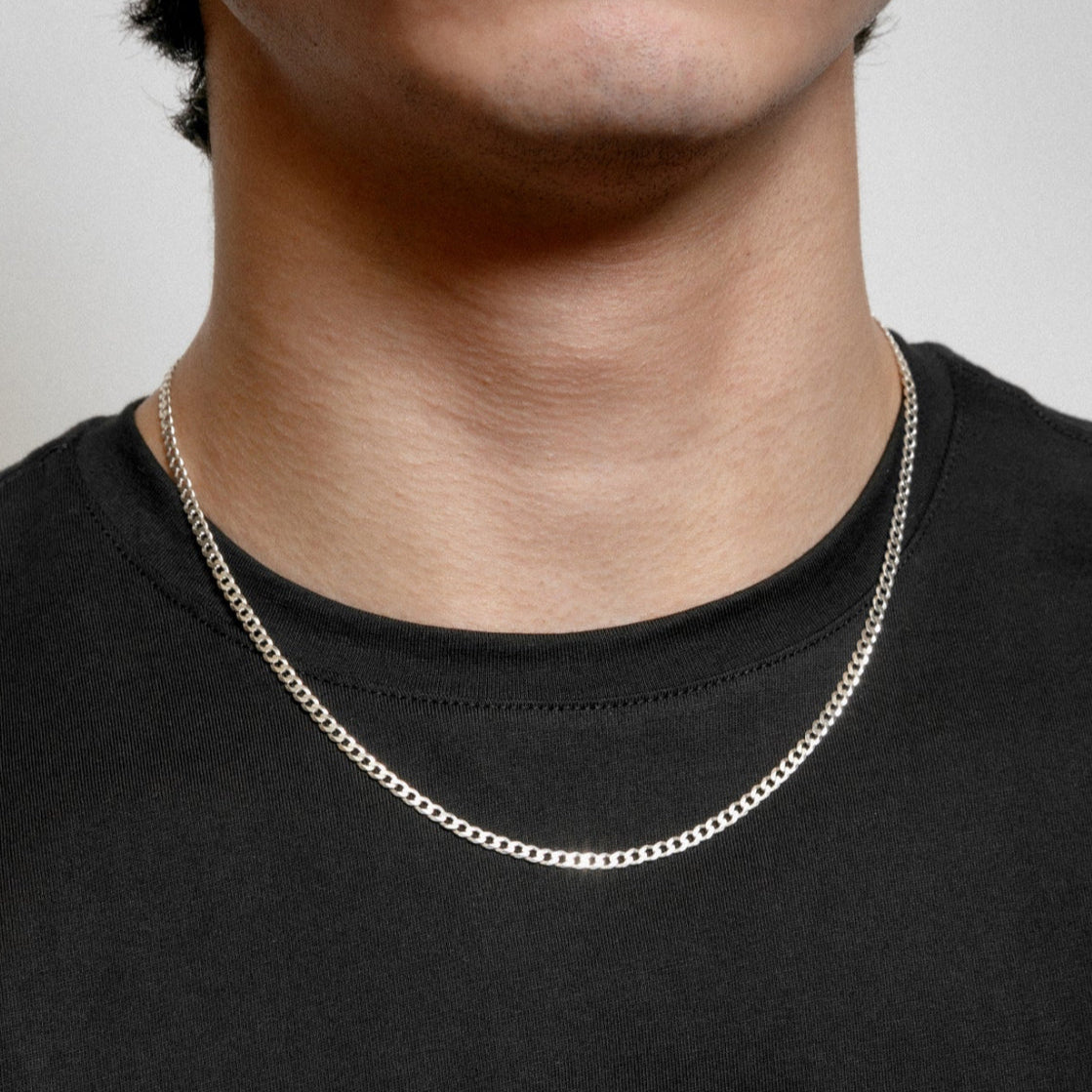 Silver chain necklace worn by a person on a plain background