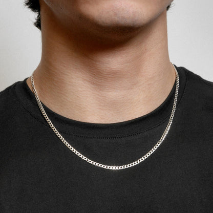 Silver chain necklace worn by a person on a plain background