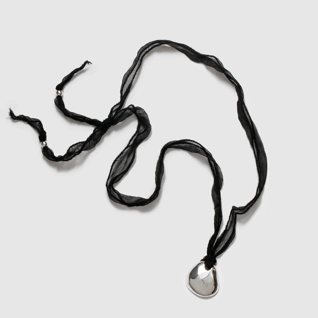 A black silk necklace with a silver plated organic pendant and sterling silver end beads.