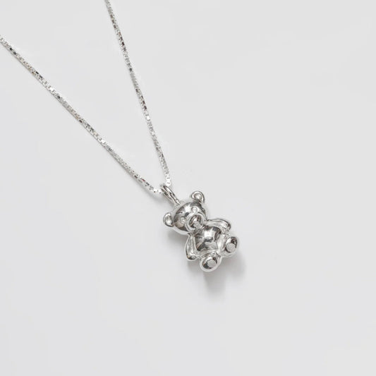 Silver teddy bear pendant necklace on a light gray background
