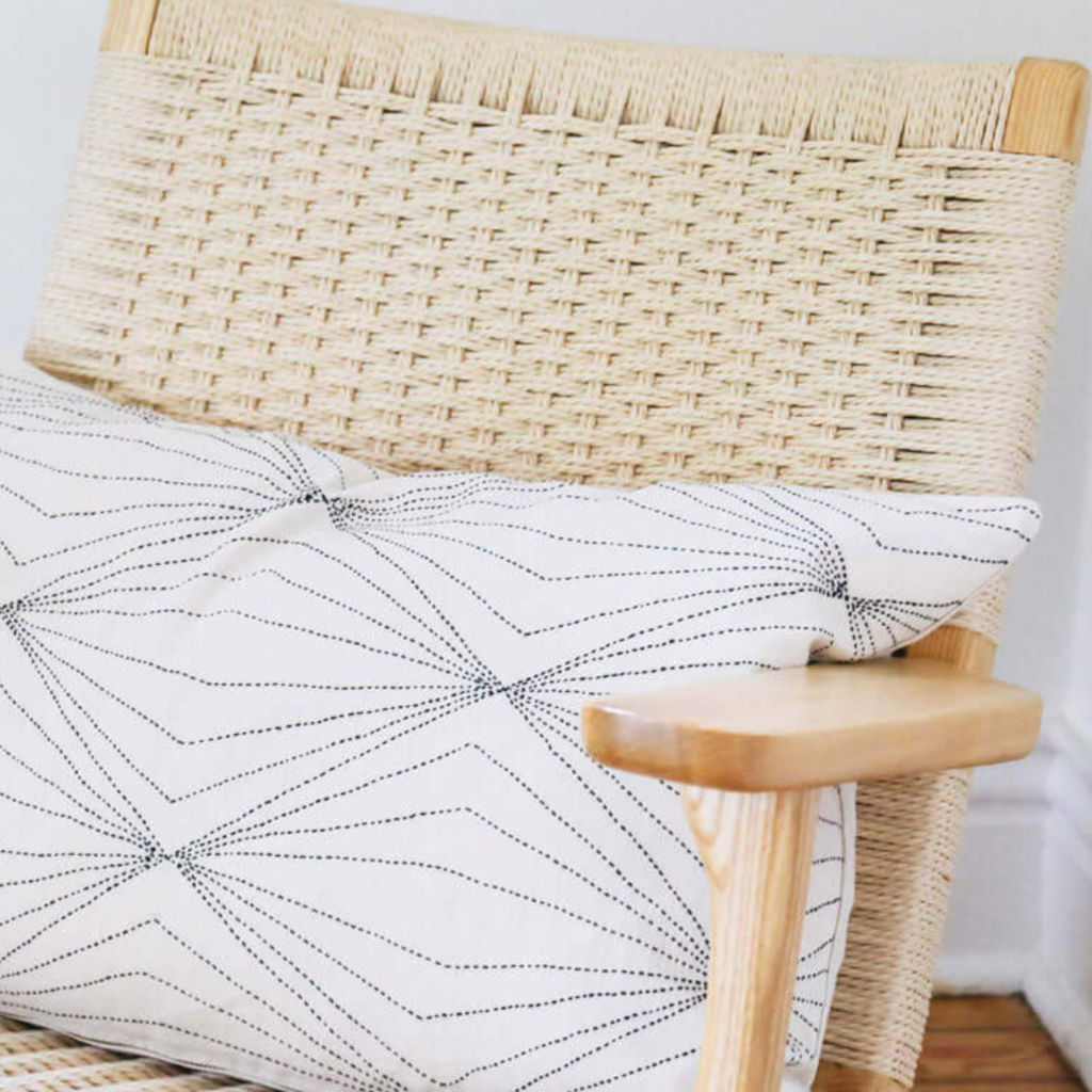 A lumbar pillow with a contemporary prism-inspired geometric embroidered pattern on a white background, placed on a chair.