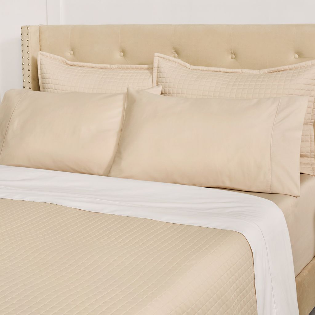 Beige bedding set with pillows on a bed against a white wall.
