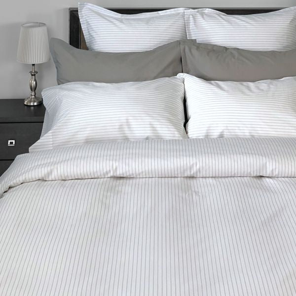 Gray striped bedding set on a bed with a nightstand and lamp in the background.