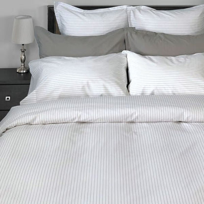 Gray striped bedding set on a bed with a nightstand and lamp in the background.