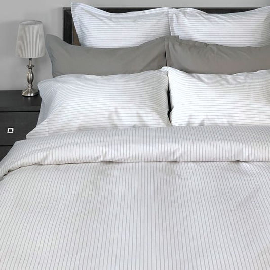 Gray striped bedding set on a bed with a nightstand and lamp in the background.