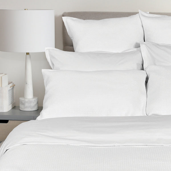 White bedding set with pillows on a bed in a bedroom setting.