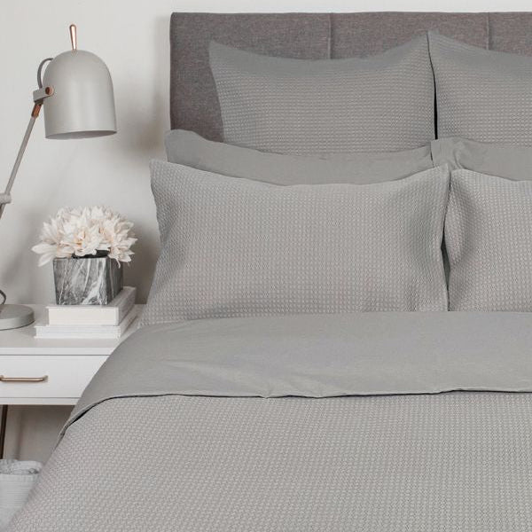 Gray textured bedding set on a bed with a nightstand and lamp in a bedroom setting.