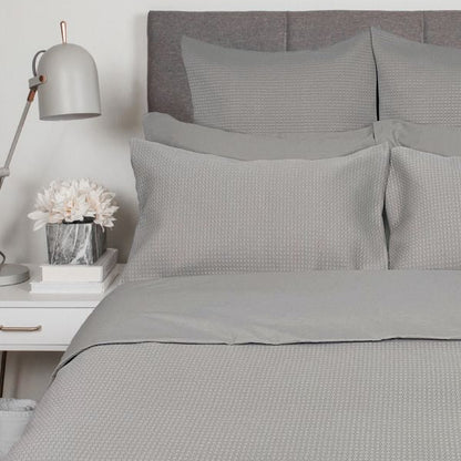 Gray textured bedding set on a bed with a nightstand and lamp in a bedroom setting.