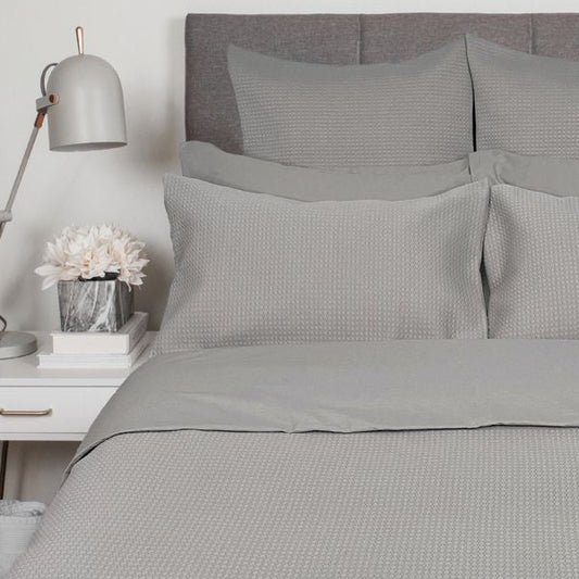 Gray textured bedding set on a bed with a nightstand and lamp in a bedroom setting.