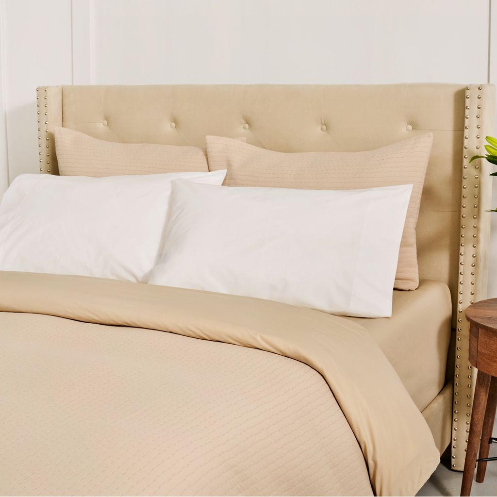 Beige bed with white pillows and a wooden side table.