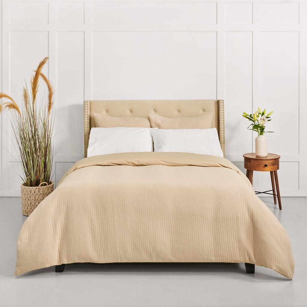 Beige bedspread on a bed with a wooden headboard in a room with plants and a side table.
