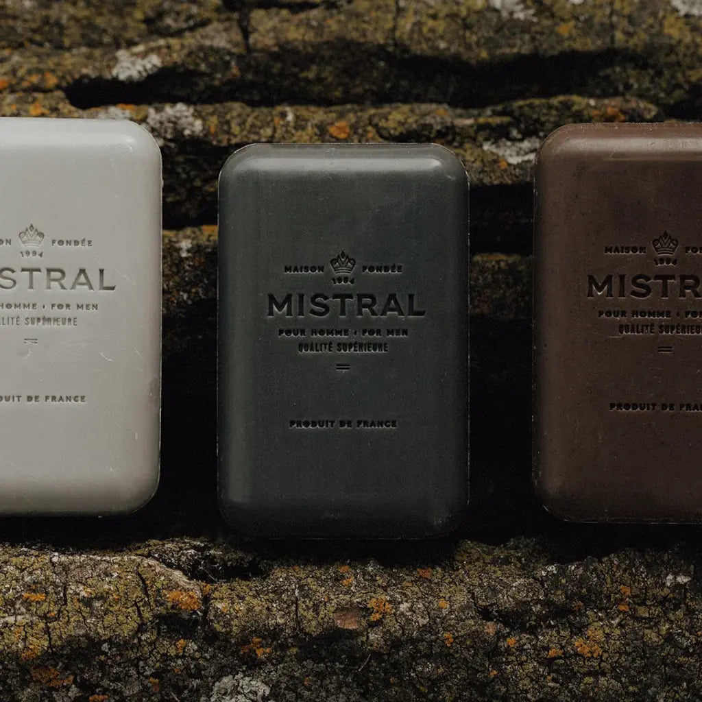 Three bars of Mistral soap in different colors against a textured stone background