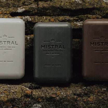 Three bars of Mistral soap in different colors against a textured stone background