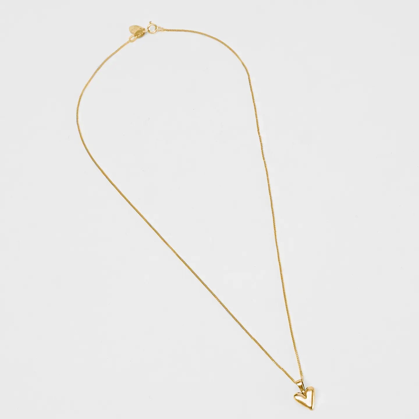 Gold necklace with a heart pendant on a light gray background