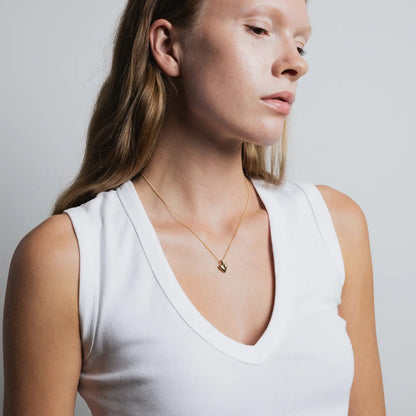 Woman wearing a white tank top and gold necklace against a plain background