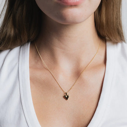 Gold necklace with a heart pendant worn by a person against a white background
