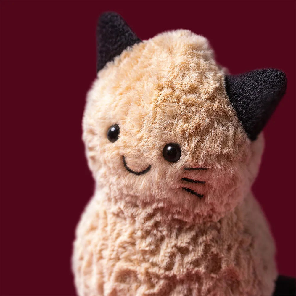 A close-up of a plush peanut toy wearing a cat costume, set against a solid dark red background.