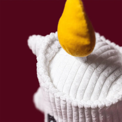A close-up of a white ribbed plush candle toy set against a solid dark red background.